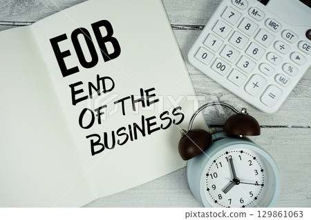 EOB End Of the Business text on paper notebook page with alarm clock and calculator on wooden background 129861063