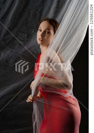 Woman posing gracefully in a studio setting, expressing deep emotion while interacting with fabric drapery Woman posing gracefully in a studio setting, expressing deep emotion while interacting with fabric drapery 129861204