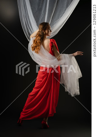 Woman in a red dress poses elegantly in a studio, showcasing emotion and grace with flowing fabric 129861213