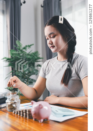 Businesswoman saving money with piggy bank and coins on desk, financial planning and investment concept. Young Asian woman making stack of coin. invest save finance concept, saving money, investment Businesswoman saving money with piggy bank and coins on desk, financial planning and investment concept. Young Asian woman making stack of coin. invest save finance concept, saving money, investment 129861277