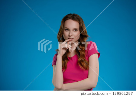 Woman poses in a studio setting with a bright blue background, expressing emotion and confidence through her stance and expression 129861297