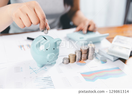 Businesswoman saving money with piggy bank and coins on desk, financial planning and investment concept. Young Asian woman making stack of coin. invest save finance concept, saving money, investment Businesswoman saving money with piggy bank and coins on desk, financial planning and investment concept. Young Asian woman making stack of coin. invest save finance concept, saving money, investment 129861314