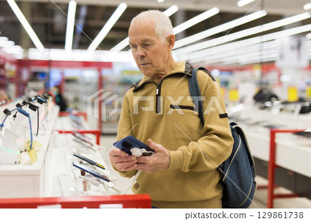 elderly man examines tablet computer in showroom of electronics store elderly man examines tablet computer in showroom of electronics store 129861738