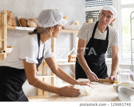 Elderly man and woman knead and roll out dough Elderly man and woman knead and roll out dough 129861748