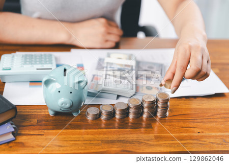 Businesswoman saving money with piggy bank and coins on desk, financial planning and investment concept. Young Asian woman making stack of coin. invest save finance concept, saving money, investment Businesswoman saving money with piggy bank and coins on desk, financial planning and investment concept. Young Asian woman making stack of coin. invest save finance concept, saving money, investment 129862046