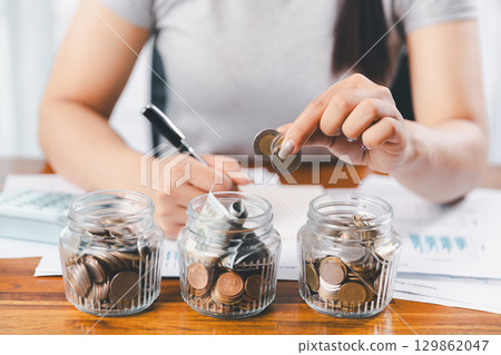 Businesswoman saving money with piggy bank and coins on desk, financial planning and investment concept. Young Asian woman making stack of coin. invest save finance concept, saving money, investment Businesswoman saving money with piggy bank and coins on desk, financial planning and investment concept. Young Asian woman making stack of coin. invest save finance concept, saving money, investment 129862047