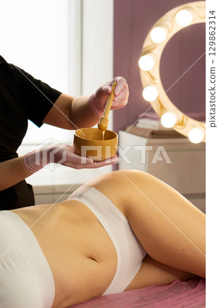 Spa therapist stirring honey mixture before applying to skin. 129862314