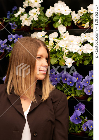 Young woman poses outdoors against colorful vertical flower wall. 129862317