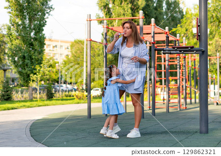 Mom Blows Bubbles While Daughter Hugs Her Legs 129862321