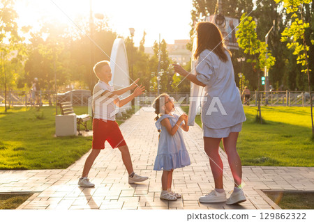 Boy and girl reach bubbles while mother blows 129862322