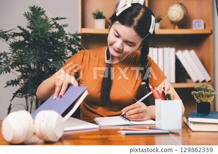 woman sitting at desk working on laptop taking notes in notebook, female studying online, watching webinar using computer, writing check list. Remote college school education, e learning concept. woman sitting at desk working on laptop taking notes in notebook, female studying online, watching webinar using computer, writing check list. Remote college school education, e learning concept. 129862339