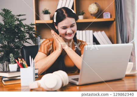 Asian girl doing homework and studying at home. woman using laptop at desk write notes watching webinar, study online, look at learn web class or having virtual call meeting remote working from home. Asian girl doing homework and studying at home. woman using laptop at desk write notes watching webinar, study online, look at learn web class or having virtual call meeting remote working from home. 129862340