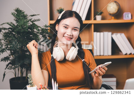 Asian girl doing homework and studying at home. woman using laptop at desk write notes watching webinar, study online, look at learn web class or having virtual call meeting remote working from home. Asian girl doing homework and studying at home. woman using laptop at desk write notes watching webinar, study online, look at learn web class or having virtual call meeting remote working from home. 129862341