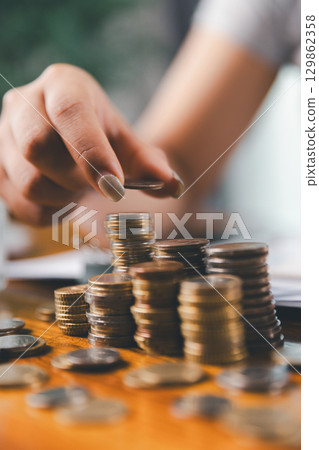 Businesswoman saving money with piggy bank and coins on desk, financial planning and investment concept. Young Asian woman making stack of coin. invest save finance concept, saving money, investment Businesswoman saving money with piggy bank and coins on desk, financial planning and investment concept. Young Asian woman making stack of coin. invest save finance concept, saving money, investment 129862358
