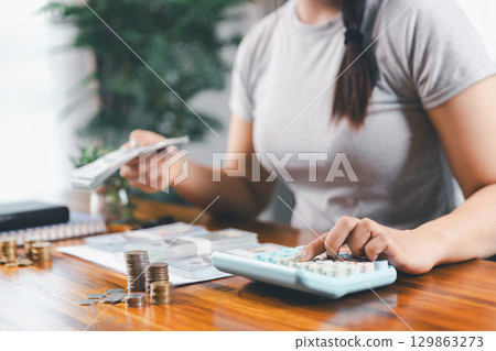 Young Asian woman making stack of coin. invest save finance concept, saving money, investment. dollar bills on table with pile of coins and banks calculator, money to save and invest to make income. Young Asian woman making stack of coin. invest save finance concept, saving money, investment. dollar bills on table with pile of coins and banks calculator, money to save and invest to make income. 129863273