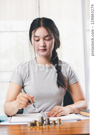Young Asian woman making stack of coin. invest save finance concept, saving money, investment. dollar bills on table with pile of coins and banks calculator, money to save and invest to make income. Young Asian woman making stack of coin. invest save finance concept, saving money, investment. dollar bills on table with pile of coins and banks calculator, money to save and invest to make income. 129863274