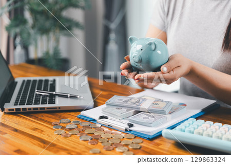 Businesswoman saving money with piggy bank and coins on desk, financial planning and investment concept. Young Asian woman making stack of coin. invest save finance concept, saving money, investment 129863324