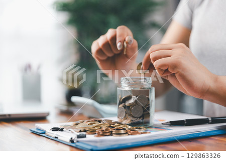 Businesswoman saving money with piggy bank and coins on desk, financial planning and investment concept. Young Asian woman making stack of coin. invest save finance concept, saving money, investment Businesswoman saving money with piggy bank and coins on desk, financial planning and investment concept. Young Asian woman making stack of coin. invest save finance concept, saving money, investment 129863326