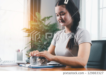 Young Asian woman making stack of coin. invest save finance concept, saving money, investment. dollar bills on table with pile of coins and banks calculator, money to save and invest to make income. Young Asian woman making stack of coin. invest save finance concept, saving money, investment. dollar bills on table with pile of coins and banks calculator, money to save and invest to make income. 129863327