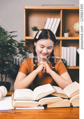 Asian girl doing homework and studying at home. woman using laptop at desk write notes watching webinar, study online, look at learn web class or having virtual call meeting remote working from home. 129863395