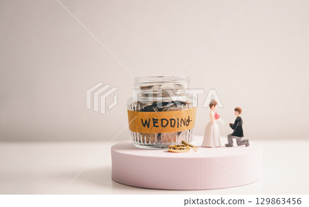 Save money for wedding and planning wedding concept. Sustainable financial goal for family life or married life. Miniature wedding on rows of rising coins, depicts savings or growth for new family. 129863456
