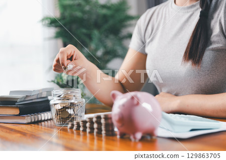 Businesswoman saving money with piggy bank and coins on desk, financial planning and investment concept. Young Asian woman making stack of coin. invest save finance concept, saving money, investment Businesswoman saving money with piggy bank and coins on desk, financial planning and investment concept. Young Asian woman making stack of coin. invest save finance concept, saving money, investment 129863705
