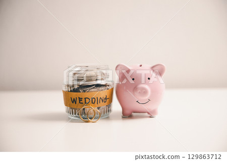 Save money for wedding and planning wedding concept. Sustainable financial goal for family life or married life. Miniature wedding on rows of rising coins, depicts savings or growth for new family. 129863712