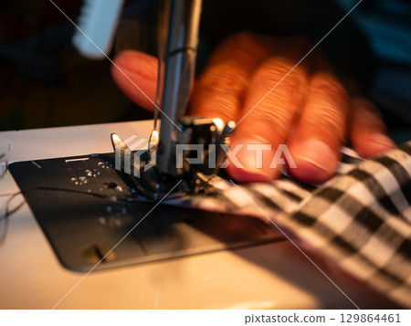 Elderly Woman Hands Sewing Fabric with Electric Sewing Machine. Senior Labor and Handicraft Work. Elderly Woman Hands Sewing Fabric with Electric Sewing Machine. Senior Labor and Handicraft Work. 129864461