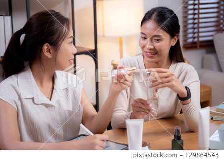 Two asian businesswoman testing and researching cosmetic product or cream in bottle in office. 129864543