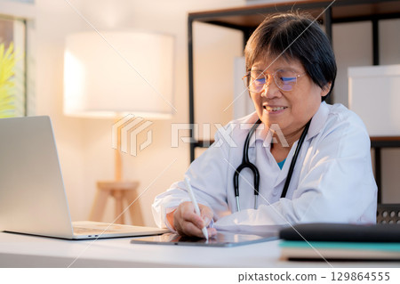 Senior asian doctor writing prescription or document on tablet in clinic office. Senior asian doctor writing prescription or document on tablet in clinic office. 129864555