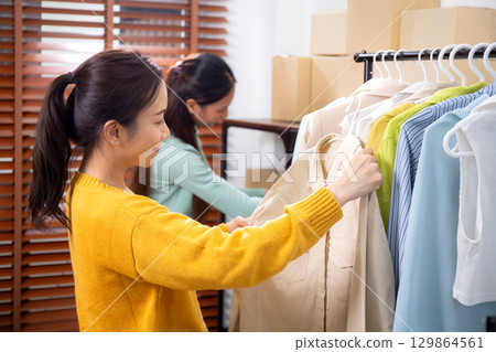 Two young asian woman arranging clothes in store for preparation delivery, seller choice clothes. 129864561