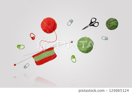 Tools for knitting warm clothes: scissors, green and red balls of thread, stoppers, and knitting needles with knitted green red piece of fabric flying in air on gray background. Hobby home crafts. Tools for knitting warm clothes: scissors, green and red balls of thread, stoppers, and knitting needles with knitted green red piece of fabric flying in air on gray background. Hobby home crafts. 129865124
