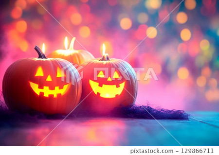 Candle lit Halloween pumpkins glowing in vibrant colors with empty space for festive greetings 129866711