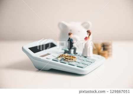 Save money for wedding and planning wedding concept. Sustainable financial goal for family life or married life. Miniature wedding on rows of rising coins, depicts savings or growth for new family. 129867051