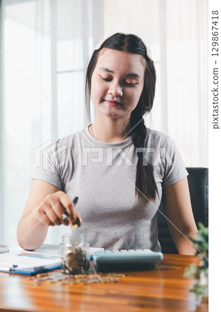 Businesswoman saving money with piggy bank and coins on desk, financial planning and investment concept. Young Asian woman making stack of coin. invest save finance concept, saving money, investment Businesswoman saving money with piggy bank and coins on desk, financial planning and investment concept. Young Asian woman making stack of coin. invest save finance concept, saving money, investment 129867418