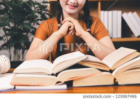 Asian girl doing homework and studying at home. woman using laptop at desk write notes watching webinar, study online, look at learn web class or having virtual call meeting remote working from home. 129867466
