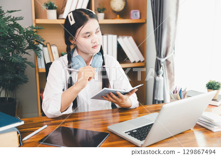 Asian girl student wear headphones learning online watching webinar class looking at laptop computer eLearning remote lesson making notes or video calling virtual conference meeting teacher at home. Asian girl student wear headphones learning online watching webinar class looking at laptop computer eLearning remote lesson making notes or video calling virtual conference meeting teacher at home. 129867494