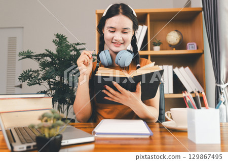 woman sitting at desk working on laptop taking notes in notebook, female studying online, watching webinar using computer, writing check list. Remote college school education, e learning concept. 129867495
