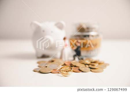 Save money for wedding and planning wedding concept. Sustainable financial goal for family life or married life. Miniature wedding on rows of rising coins, depicts savings or growth for new family. 129867499