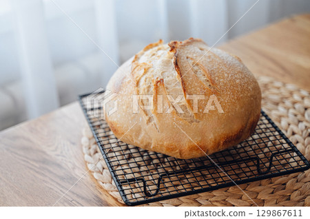 Homemade sourdough bread cooling on a rack on a rustic wooden table 129867611