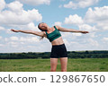 A sporty girl stands among the green grass on a sunny summer day. 129867650