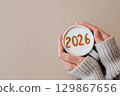 Woman in cozy sweater holding hot coffee with 2026 on milk foam, festive New Year concept 129867656