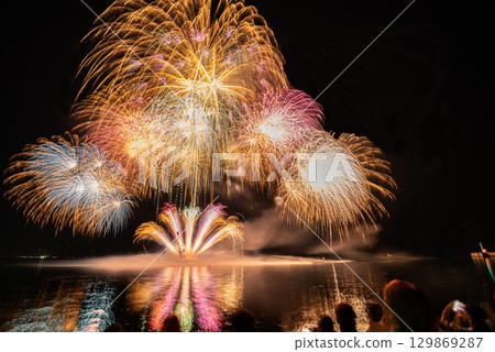 People looking up at large fireworks on the beach 129869287