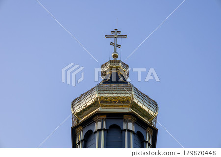 A gleaming cross decorates the top of a church dome under bright sunlight, showcasing intricate architectural details A gleaming cross decorates the top of a church dome under bright sunlight, showcasing intricate architectural details 129870448