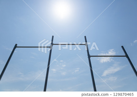 Metal scaffolding stands against a clear blue sky with sunlight illuminating the scene and soft white clouds in the background 129870465