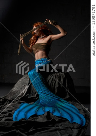 Young mermaid holding cloth in dark studio 129871791