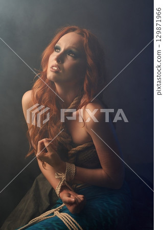 Frightened redheaded mermaid tied with ropes 129871966