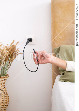 Woman holding charger cable with plug in the socket. 129872823