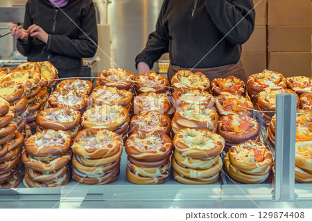 Stacks of soft pretzel rings filled with melted cheese, bacon, and toppings at vendor stall. Concept of pretzel snacks, savory bakery, holiday snack, holiday fair food Stacks of soft pretzel rings filled with melted cheese, bacon, and toppings at vendor stall. Concept of pretzel snacks, savory bakery, holiday snack, holiday fair food 129874408