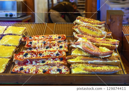 Hot sandwiches with melted cheese, sausages, pizza toppings displayed at festive food stall. Concept of Christmas cheese sandwich, quick meal, winter comfort street food Hot sandwiches with melted cheese, sausages, pizza toppings displayed at festive food stall. Concept of Christmas cheese sandwich, quick meal, winter comfort street food 129874411